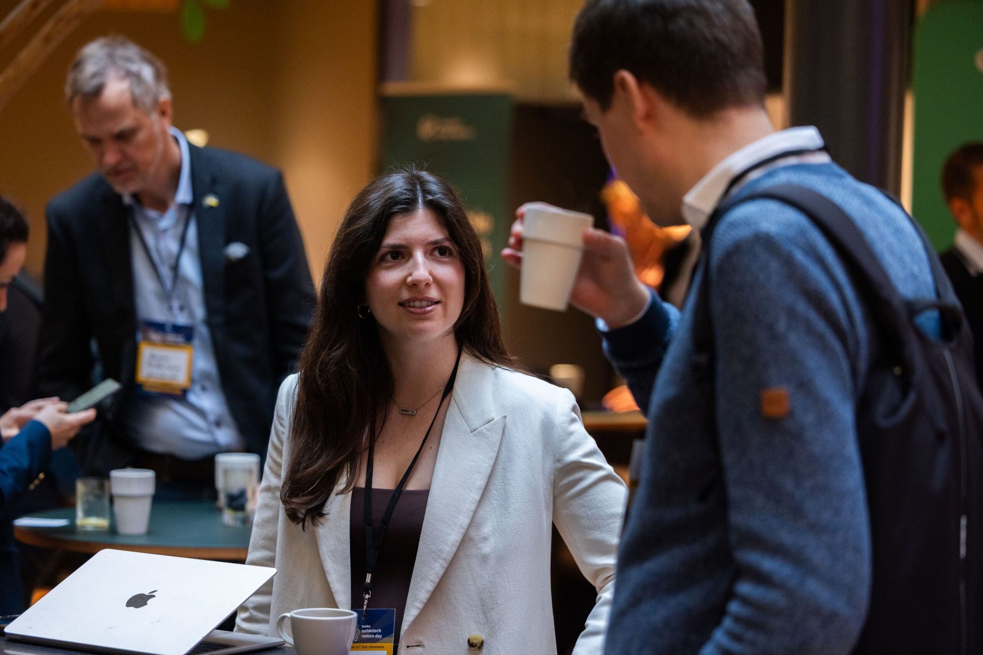 A woman in a white blazer speaks with a delegate holding a coffee cup during event networking