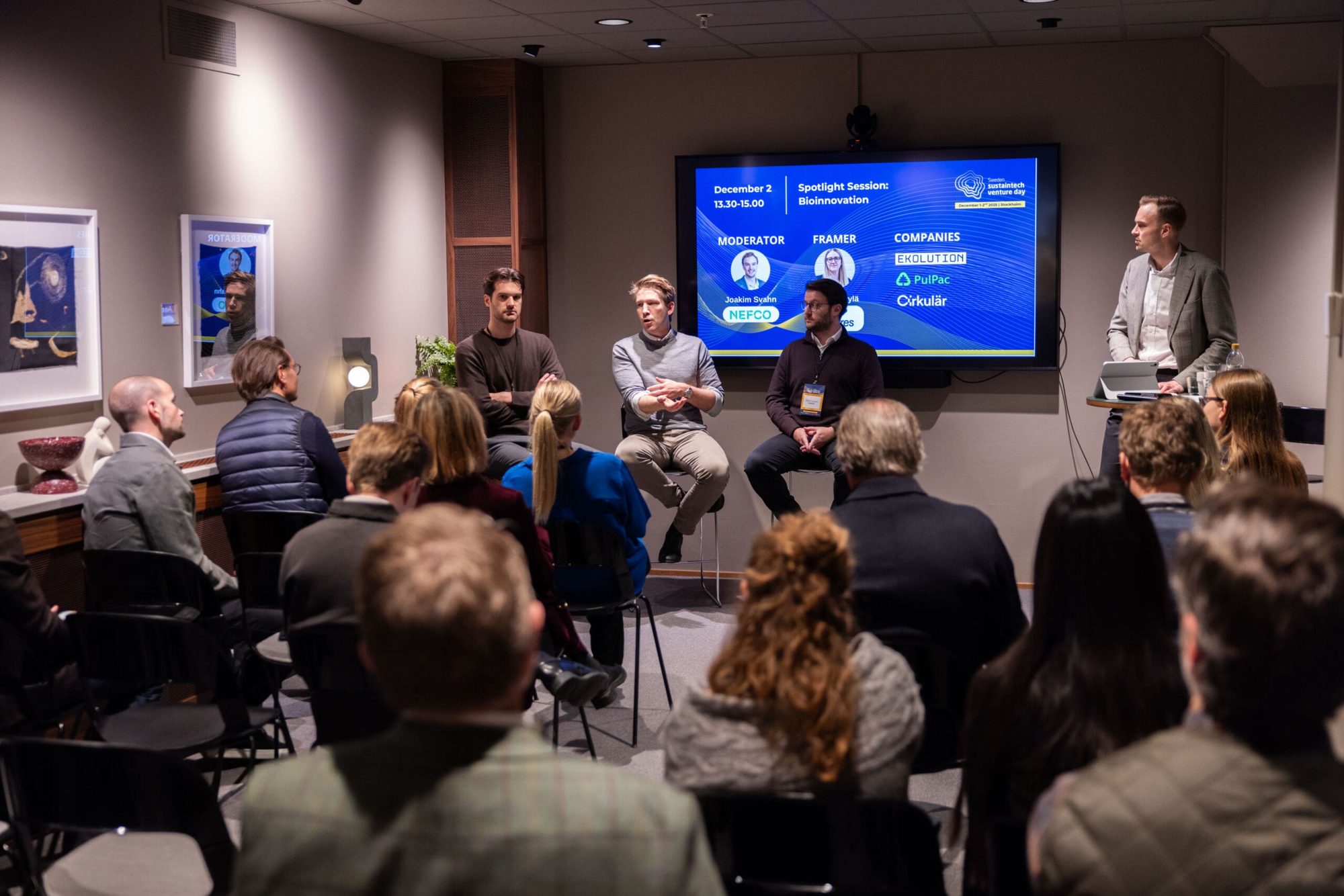 A seated audience listens to a four-person bioinnovation panel